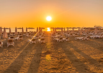tranqiul sunrise an a beautiful beach with umbrellas on thr foreground , golden sand and sun rays and calm sea on the background