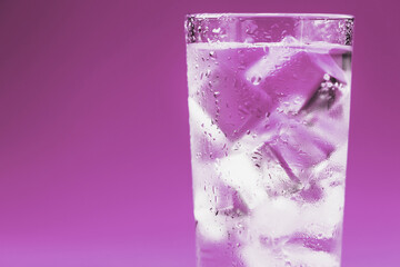 Glass with water and ice cubes on a pink background