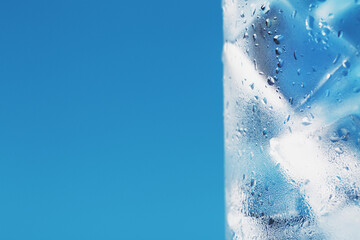 Ice cubes in a glass with refreshing ice water on a blue background.