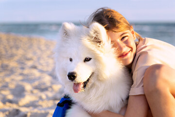 The dog is a friend of the child. A teenage girl hugs a dog, a white Samoyed husky on the seashore.  Pets, friendship with animals concept.