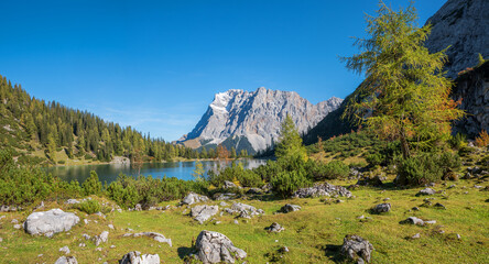 alpine landscape Seebensee, Zugspitze mountain. lake shore with rocks and larch trees, autumn in...