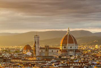 Fototapeta na wymiar Florence's beautiful Gothic cathedral standing out over the surrounding city buildings, with the mountains in the background at sunset