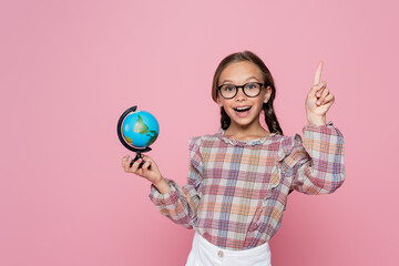 amazed girl with small globe showing idea gesture while looking at camera isolated on pink