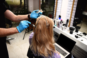 Hairdresser applying chemical color dye onto hair of customer, a businesswoman working on laptop in salon