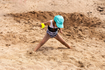 Child in swimsuit and a cap plays in the sand by the sea.