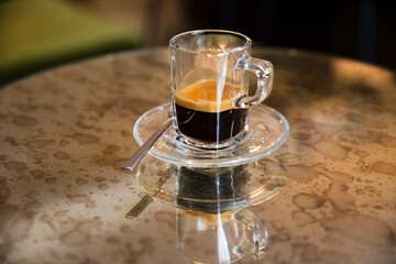 Close up of a glass cup of espresso on fancy stained mirror table. 