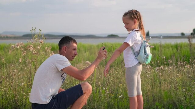 Father sprays mosquito spray on his child's arms. A man is treating the skin of a child from insect mowing.