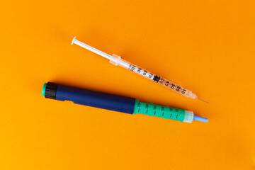 Injectable pen and insulin syringe on an orange background