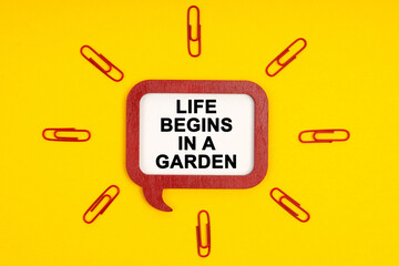 On a yellow background, paper clips and a mental plaque with the inscription - Life Begins In A Garden