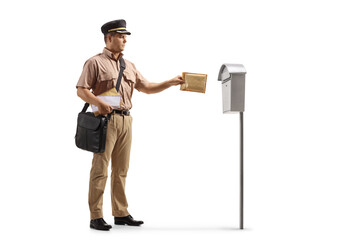Full length shot of a mailman in a uniform putting a letter into a mail box - obrazy, fototapety, plakaty