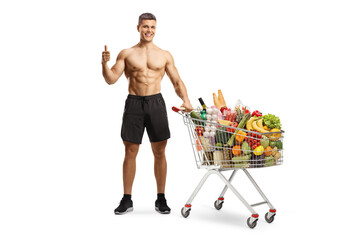 Shirtless sporty man with a shopping cart full of food showing thumbs up