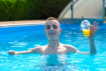 Young smiling guy with an amputated arm drinks a cocktail in swimming pool in the courtyard of his...