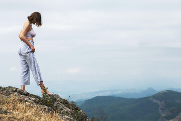 Young woman with short hair walks through the mountains in the early morning, outdoors, relaxes, general plan, mountains in the background