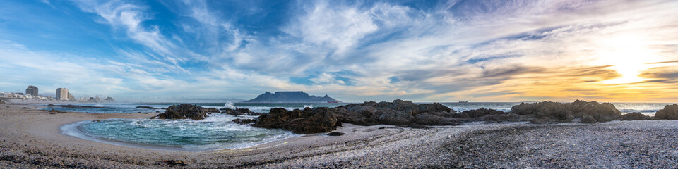 Scenic sunset beach vista of Table Mountain, Cape Town, South Africa. A stunning view from Table View beach - across the bay where tourists and surfers alike come to enjoy the beach and ocean.	