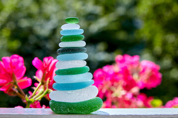 A pyramid of glass stones from the beach on a background of red flowers
