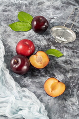 Fresh ripe purple plum fruits  whole and slices and leaves  scattered on grey white stone