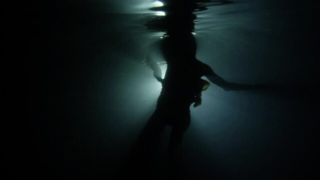 Woman dances underwater in silhouette