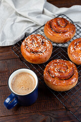 Freshly baked traditional Swedish cinnamon buns Kanelbulle with cup of coffee or cappuccino, on wooden background, vertical