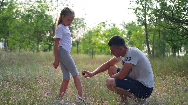A father sprays a mosquito spray on a child's legs. Male hands treat the baby's skin from insect mows.