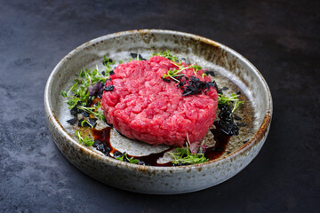 Modern style gourmet tartar raw from beef filet with herbs and spices served as close-up on a...