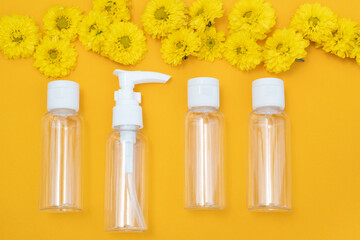 composition of small travelling bottles and jars for cosmetic products on yellow background and yellow flowers