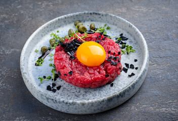 Modern style gourmet tartar raw from beef filet with egg and capers served as close-up on a Nordic design plate with copy space