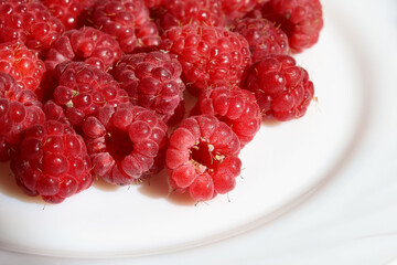 Red ripe raspberry berries on white plate