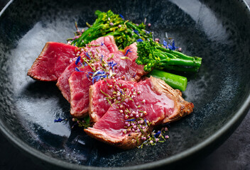Modern style baby broccoli with fried dry aged sliced beef fillet steak served as close-up on a...