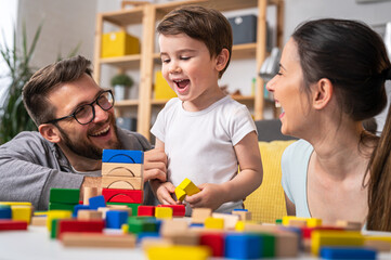 Fototapeta premium Young happy family. Mother and father playing with her cute toddler son at home using didactic wooden toys. Home education