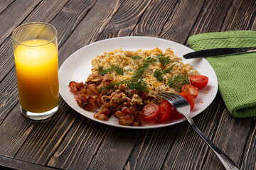 Orange juice and scrambled eggs with bacon and tomatoes on a wooden table