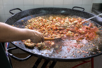 start of preparation of a paella with a base or sofrito of onion tomato chicken meat in a large paella pan with selective focus