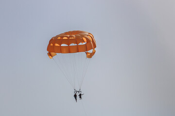 Orange Parachute High In The Sky With Two People On The Parasailing