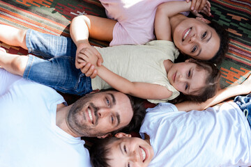 Two children and two parents lie together on a colorful embroidered carpet, resting after a busy day during summer vacation