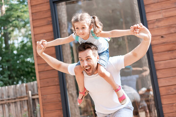 Dad runs, plays with his daughter sitting on his shoulders, dad holds the girl's hands, they have fun during a summer walk together.