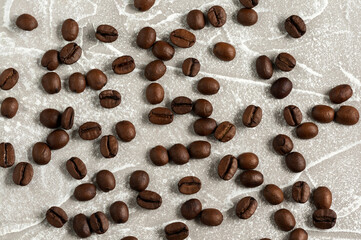 Brown roasted coffee beans scattered on gray marble background. View from above. Flat lay.