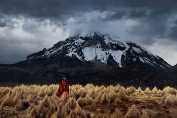 An altiplano woman walks by Nevado Sajama--Bolivia's highest mountain--its peak shrouded in dramatic clouds.  - 447976067