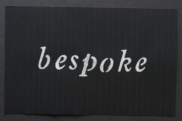 the word "bespoke" loosely stencilled on black notepad paper and arranged on a dark gray paper background 
