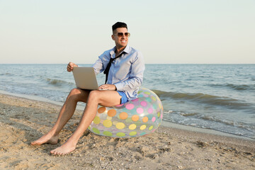 Happy businessman working with laptop on beach. Business trip