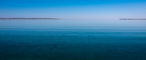 Seascape of harbor entrance jetties in distance in Hyannis. Horizon, blue seawater, blue sky, and white light reflections.