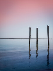 Seascape with three pilings. Abstract minimalist image of the horizon and vertical poles. Pink...