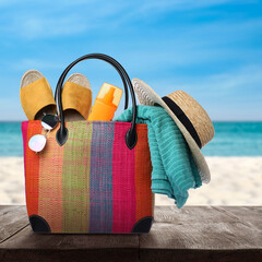 Stylish bag with beach accessories on wooden surface near seashore