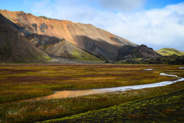 Grassy meadows and a small river on a valley surrounded by the colorful rhyolite mountains of...