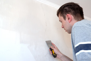 Construction man worker repairing a crack wall of a home, plastering cement on wall. Builder...