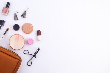 Top view. A set of women's make-up kits, eyelash curler, face powder, lipstick, earrings, brush are outside a brown bag on a white background and space for captions.