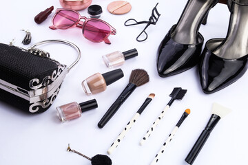 Looks close. A set of women's makeup and fashion accessories. Eyelash curler, face powder, lipstick, 
earrings, brush, high heels, handbag, and stylish glasses on white background.
