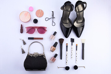 Top view. A set of women's makeup and fashion accessories. Eyelash curler, face powder, lipstick, earrings, brush, high heels, handbag, and stylish glasses are on a white background.