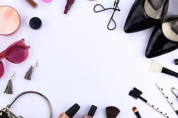 Top view. Circle-shaped women's make-up and accessories. Eyelash curler, face powder, lipstick,
earrings, brush, high heels, handbag, and stylish glasses on a white background and space for text.