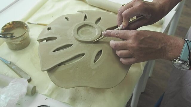Woman hand potter making clay monstera leaf in pottery workshop studio. Process of creating ceramic vase. Handmade, hobby art and handicraft concept.