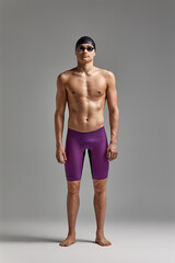 Young swimmer in excellent physical shape in full growth on a gray background with copy space, call...