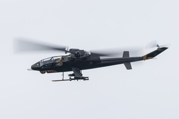 The shape of an AH-1 Cobra attack helicopter (in Vietnam war color scheme, with shark teeth)  against the sky, with rockets and machine gun